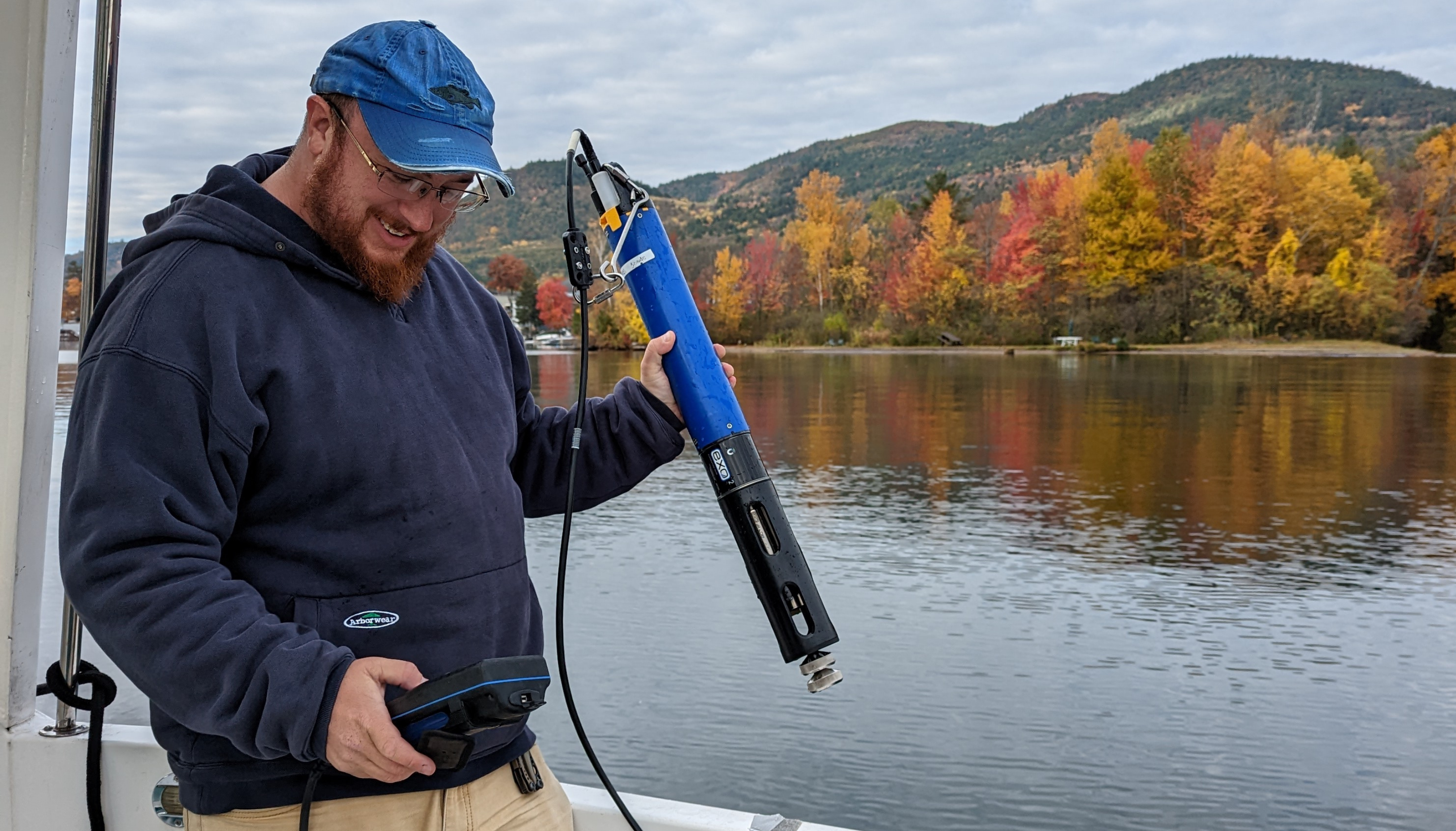 Researcher preparing to use water quality sensor pod with lake in the background
